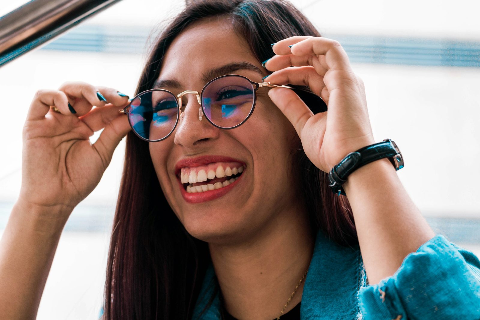 A woman laughing as she adjusts a new pair of glasses.